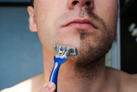 Male shaved off half the beard. Chin closeup with a razor for smooth skinの写真素材