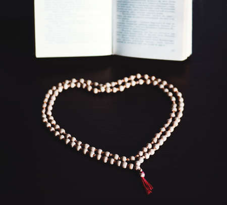 Old wooden rosary beads on a book of ceremonies. photo with copy space. rosary folded in the shape of a heartの写真素材