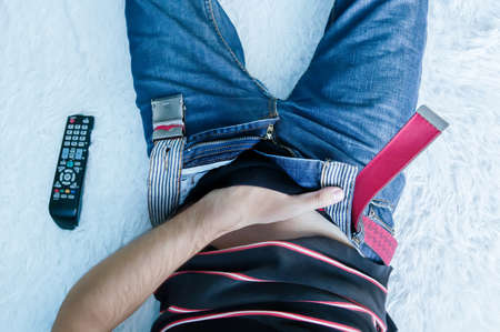 guy watches pornographic movies on TV in the bed at home. man puts his hand in your pants unbuttoned jeans.の写真素材