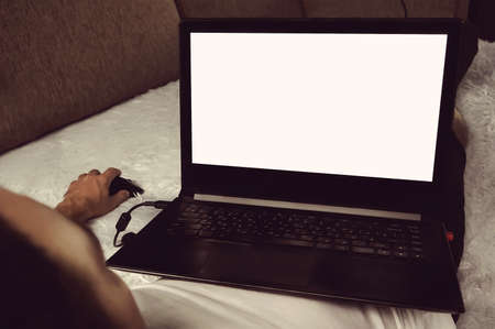Young man relaxing on the sofa with a laptop. Freelancer Lefty works at a computer at home lying in bed. Blank screen monitor for design layoutsの写真素材