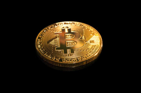 Golden Bitcoin on a black background close-up. The symbol of the modern cryptocurrency in the form of brilliant metallic coins on a black mirror reflecting surface.の写真素材