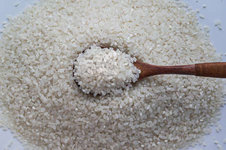 crude, uncooked rice in a small handful with wood spoonの写真素材