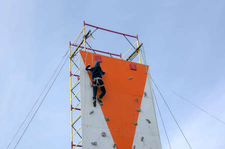 little boy climbing a rock wall indoor. vertical climbing wall on the sky backgroundの写真素材
