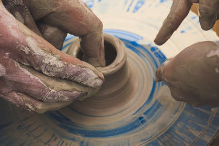 Creating a Pitcher of white clay close-up. Two pairs of hands smeared in clay making clay jug macro. The sculptor teaches children how to make a jug of clay Twisted potter's wheel.の写真素材