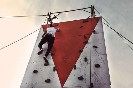 Sporty young woman training in a colorful climbing gym. Free climber girl climbing up outdoors on blue sky backgroundの写真素材