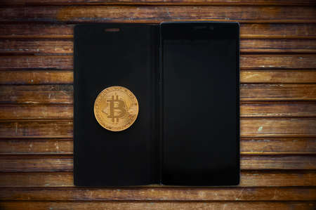 Gold bitcoin cryptocurrency with a smartphone on a wooden table. Electronic money mining concept....
