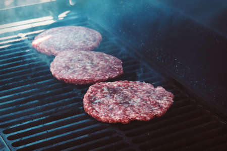 Burgers for the hamburger on Grill with Flames Cooked to Perfection. Meat beef on the grillの写真素材