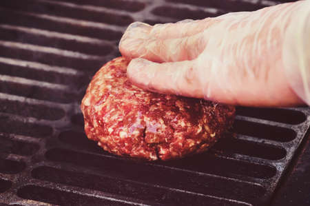 Chef making hamburger patty in kitchen with ground beef. Hand cook in a clean white sterile glove, close-up touches the cutlet grilled hamburger. The process of making the toppings for a Burgerの写真素材