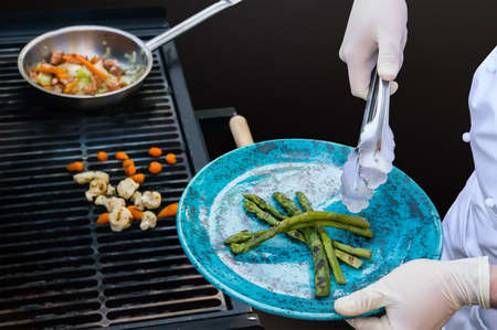 Tongs cook removes the beans on a blue plate with black grill against the process gotowki vegetables on the grill. Hands of a chef in white gloves holding a plateの写真素材