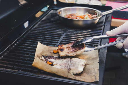 Hand of man take cooking of fish with vegetable grill, Chef cooking wagyu fish restaurant. Portionally fried pieces of fish on baking paper on the background pans with vegetables.の写真素材