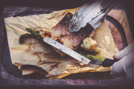 Process of cooking fish. hands cooks in clean white gloves puts grilled the fish on the paper lying on the Board.の写真素材