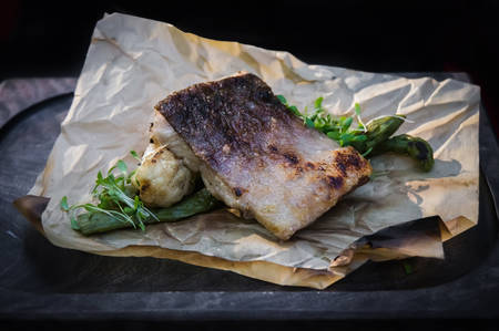 Barbecue fish Steak on Plate decorative Board with kitchen paper. on black isolated background. Beautiful restaurant supply delicacyの写真素材