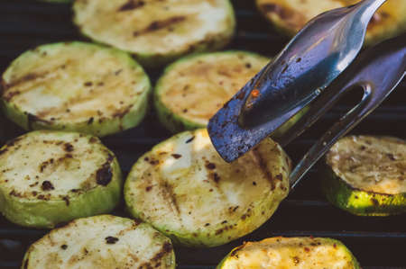 Zucchini grill spices kitchen Vegetables menu Tavern. The hands of the cooks flip grilled courgettes metal tongs on the background delicious zucchini with a delicious crust. Healthy wholesome foodの写真素材