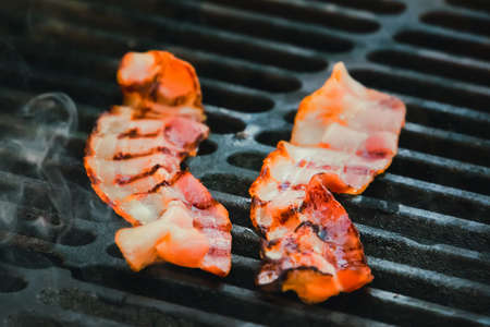 Grilled bacon skewers on a black background. Delicious strips of fatty ham on a hot grill. The ingredients for the sandwich. English Breakfastの写真素材