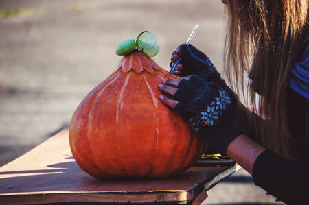 all saints day. Prepares jack-o-lantern for Halloween. Decoration for party. The female at a table on the outdoor carves their pumpkin decorative figure of Jackolantern.の写真素材
