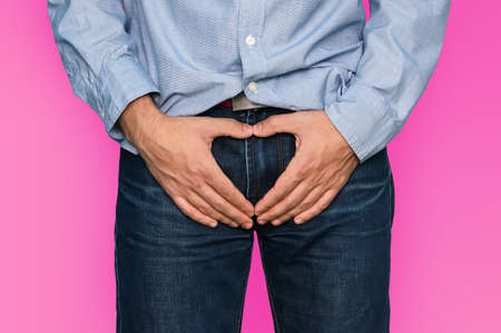 The guy has his hands on the testicles with folded hands in the shape of a heart on a pink background. A symbol of love and sexuality.の写真素材