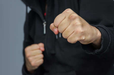 hand to hand combat. Street fist-fighter. Male fist closeup. fighter in a black hoodie prepares to strike with his fist.の写真素材