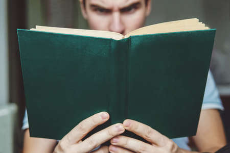 The man enjoys reading the green book. Book closeup in the hands of a young guy. The surprise on her face.の写真素材