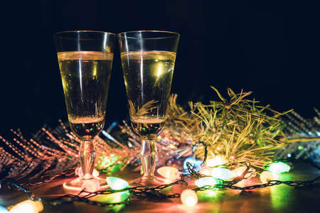 Two Glasses with champagne on a wooden table decorated with Christmas accessories to celebrate the new year and Christmas. Romantic evening. The glow from the garlandsの写真素材
