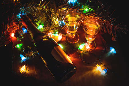 Two Glasses with champagne and bottle on a wooden table decorated with Christmas accessories to celebrate the new year and Christmas. Romantic evening. The glow from the garlands. Valentine's Dayの写真素材