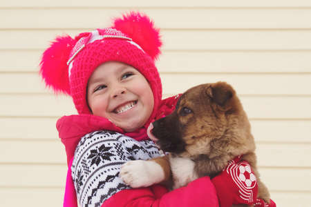 Portrait of happy child with dog in winter day. Puppy dog licks the girl's face. Winter walk with the dog. Happy child hugs your pet. Joyful embrace.の写真素材