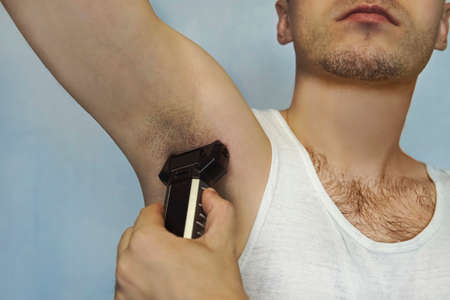 Male Beauty. Body waxing with the electric shaver. the self-care concept. Shaving the underarms. epilation clipperの写真素材