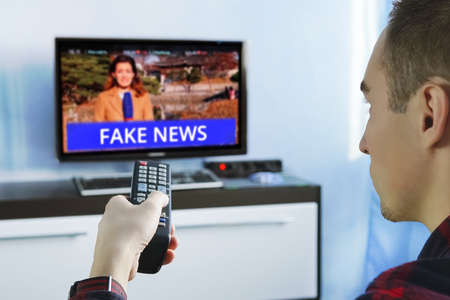 Fake News Propaganda HOAX Political TV Internet Social. young man watching the fake news report on...