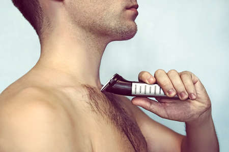 Handsome young bearded man with a trimmer shaving off body hairの写真素材