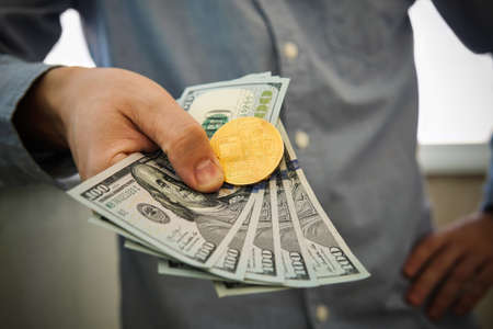 Young businessman holding dollars and coin of bitcoin in hand. Profit from trading bitcoins.の写真素材