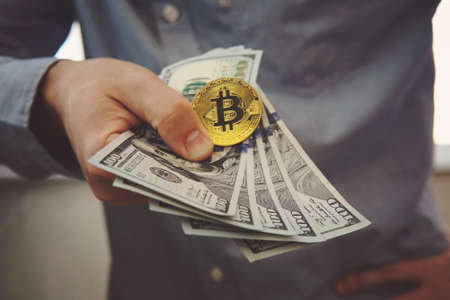 two golden Bitcoin on US dollars in a man hand. Digitall symbol of a new virtual currency.Electronic money exchange concept.の写真素材