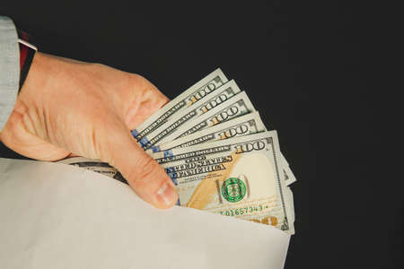 Closeup of man's hands with envelope full of dollar banknotes on wooden background. Concept of...