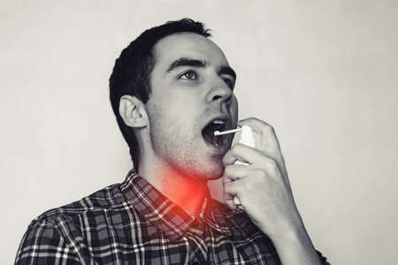 Young guy cures his throat. The man splashes into the throat spray. inflammation in the throat. The...