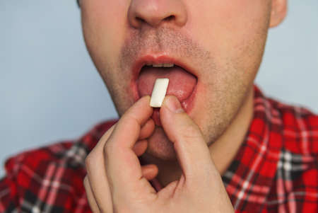 Young funny guy with chewing gum. fresh breath. Bad breath. To quit Smoking using the gum. brush up. Brushing your teeth after meals with gum. man puts his open mouth in white cushion gum closeup.の写真素材