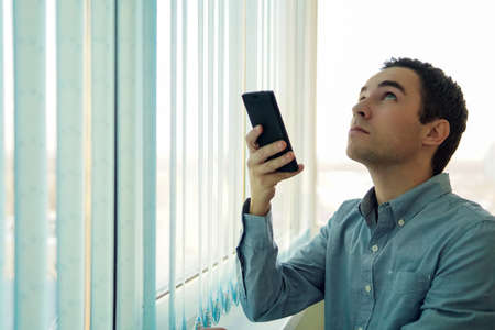 Young man using a smartphone in front of a window.