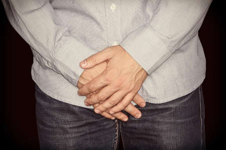 The man stands with arms crossed at groin level on black isolated background.