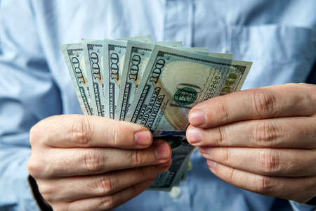 man counting five hundred US dollars. The businessman thinks of profit. Dollar bills in the hands of men on the background of blue business shirt. Success, motivation, financial flows, wealth.の写真素材