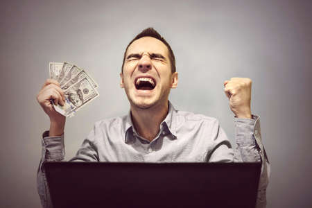 man is happy in front of the computer to hold 500 dollars. Winning in an online casino. Profit from online stock trading. Easy money. Earnings on the Internet.の写真素材