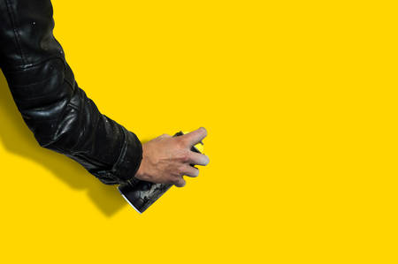 Human hands holding a graffiti Spray can. guy in the black jacket with a graffiti spray on yellow isolated background. Yellow colorの写真素材