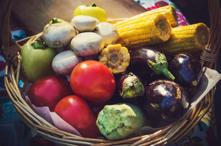 Vegetables in wicker basket. Autumn harvest: zucchini, mushrooms, eggplant, tomatoes and corn in wicker basketの写真素材