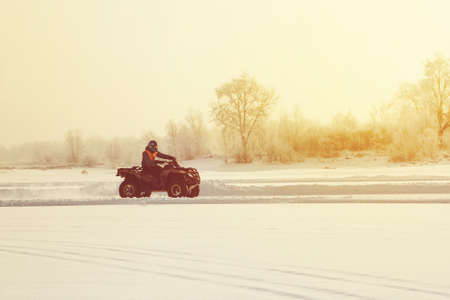 The ATV rider rides on the ice at sunset in winter, in winter the frozen lake. Winter riding on motorbikes. cold extreme. beautiful nature winterの写真素材
