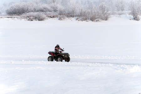 quad bike on a winter road in a field at sunset. focus on quad bike. snow drifts in the field on nature.の写真素材
