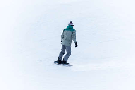 Amateur snowboarder rolls down mountain, rear view. Rear view of sportsman with snowboard. dabbler