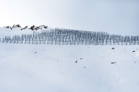 Avalanche protection construction on top of a mountain in winter. Snowy mountains with barriers in the form of fences. Barriers from a snow blockage in mountainsの写真素材