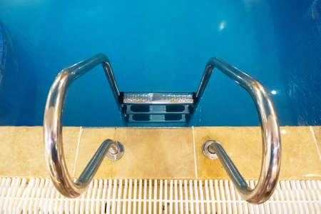 Part of swimming pool with ladder and reflected lights. An indoor pool, indoors.の写真素材