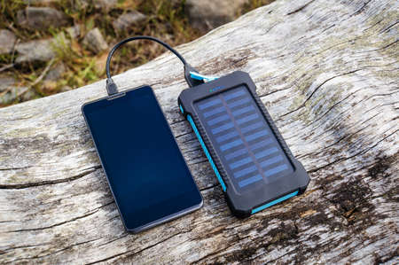 Smartphone charging with pink power bank with solar battery on wood background, selective focus and soft focusの写真素材