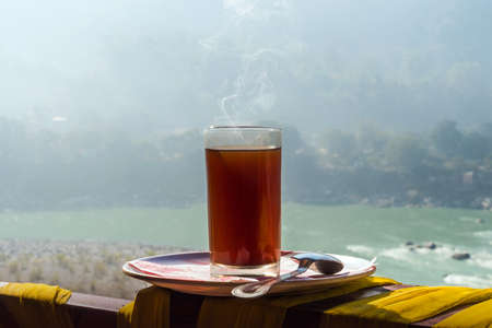 A glass of Indian tea on a saucer. The morning Breakfast in the mountains of the Himalayas. Rishikesh India. Abstract a cup of coffee with the river, the swamp, the mountain, ganga, river gangesの写真素材