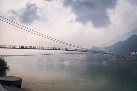 bridge Lakshman Jhula over the river Ganges in the city of rishies, India. evening dark landscape. Houses on the high slopes of the Himalayasの写真素材