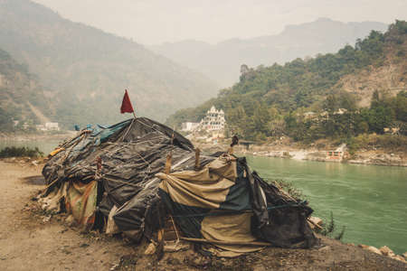 Beggar's hut by the river Ganges Rishikesh on the background of a large expensive temple. lower caste. Social inequality. The problem of poverty and the caste system of India