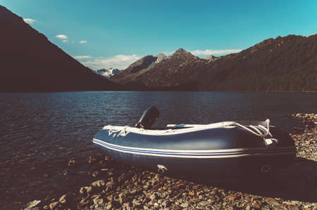 Inflatable boat with motor on the bank of a mountain river. Fishing boat on the background of beautiful mountainsの写真素材