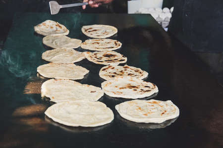 Indian chapatti on fire, Pushkar, India Close up. Fried tortillas on a hot baking sheet. Street food. Naan. Traditional street food vendor. Man cooks and inverts indian flatbreads, served with curry.の写真素材